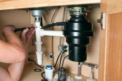 Plumber repairing a garbage disposal beneath a kitchen sink in Haverford
