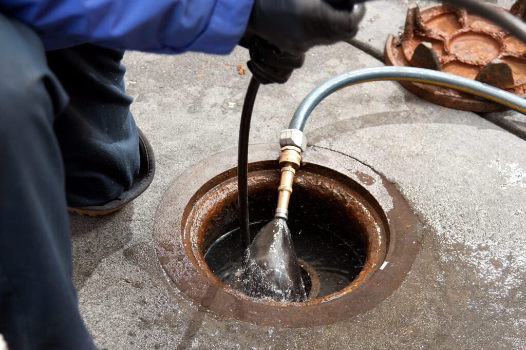 Plumber hydro jetting a sewer line through a manhole in Haverford